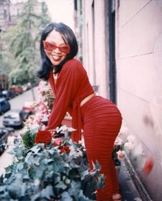 a woman in red is leaning over a planter with flowers on the side walk