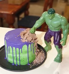 a hulk cake with purple and green icing next to a toy figure on a table