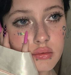 a woman with pink nails and piercings holding her hand up to her face while looking at the camera