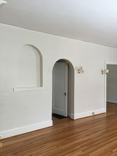 an empty living room with hard wood floors and white walls, arched doorways to the left