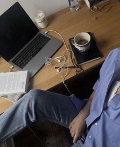 a man sitting in front of a laptop computer on top of a wooden desk next to a cup of coffee