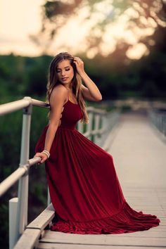 a woman in a long red dress leaning on a wooden bridge with her hands behind her head