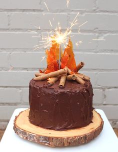 a chocolate cake with cinnamon sticks and sparklers in the middle on a wooden slice