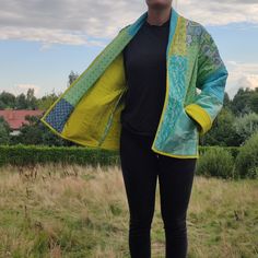 a woman standing in a field with her hands on her hips wearing a blue and yellow jacket