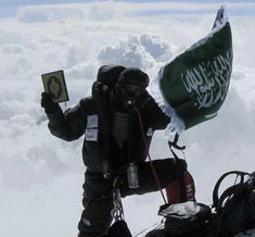 a man standing on top of a snow covered ski slope holding a green and white flag