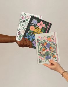 two hands are holding cards with flowers on them and one hand is reaching for the card