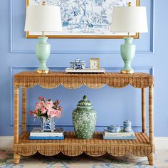 a table with two vases on it in front of a blue wall and painting