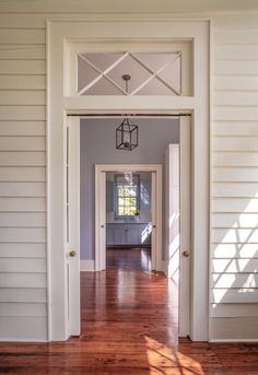 an open door leading to a hallway with hard wood flooring and white siding on the walls