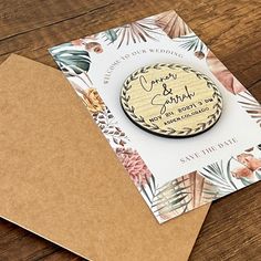 a wooden save the date magnet on top of an envelope with flowers and leaves around it