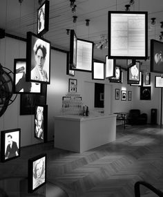 black and white photograph of an art gallery with many framed photographs on the wall, including portraits of people