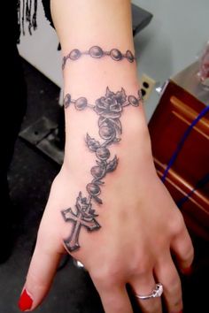 a woman's hand with a cross and rosary tattoo on her left wrist is shown