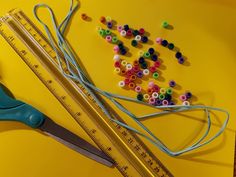 the scissors are next to some beads and thread on a yellow surface with measuring tape