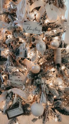 a decorated christmas tree with white and silver ornaments on the top, along with personalized tags