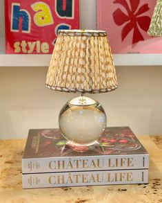 a lamp sitting on top of a stack of books next to a lamp shade that reads chateau life