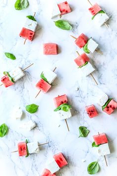 watermelon and feta skewers with basil leaves on them, sitting on a marble surface