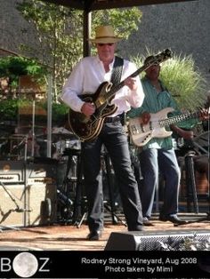 the man is playing his guitar on the stage with other musicians in the back ground