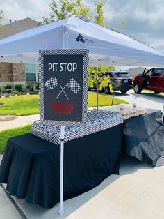 a table with a sign that says pit stop and two crossed sticks on it under a tent