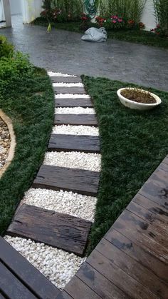 a walkway made out of wood and white pebbles leading to a potted planter