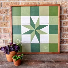 two potted plants are sitting next to a green and white quilted wall hanging