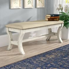 a white bench sitting on top of a wooden floor next to a blue rug and potted plant