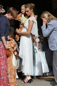 a woman in a white dress is holding a teddy bear and standing next to other people