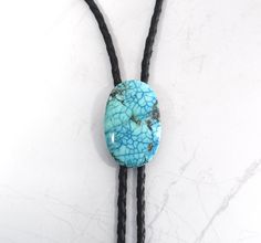 a necklace with a turquoise bead and black cord on top of a white surface