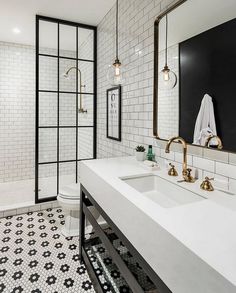 a bathroom with black and white tile, gold faucets, two sinks and a large mirror