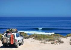 an suv parked on the beach with surfboards and backpacks strapped to it's roof