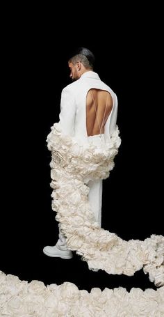 a man in a white suit standing on top of a pile of flowers with his back to the camera