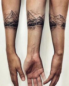 two hands holding each other with mountains and trees tattooed on their arms, both showing the same