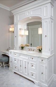 a large white bathroom vanity with two sinks and flowers in vases on the counter