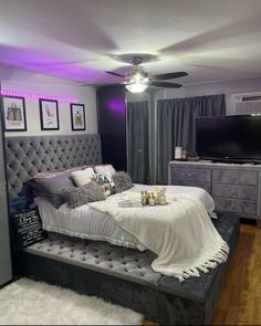 a bedroom with a bed, dresser and tv in the corner is lit up by purple lights