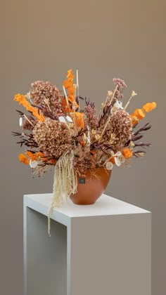 an arrangement of dried flowers in a vase on a white pedestal against a gray background