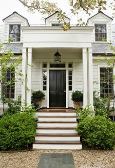 a white house with steps leading up to the front door and entryway that is flanked by bushes