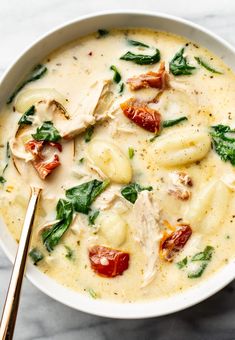 a white bowl filled with pasta and spinach covered in cheese, sauce and tomatoes