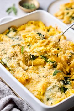 a casserole dish with spinach and cheese being spooned into the casserole