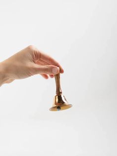 a person's hand holding a golden bell on a white background with the bell being held up