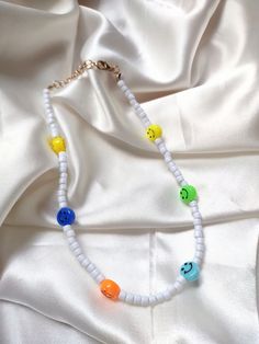 Multi-colored beaded smiley face necklace with lobster-claw closure. Adjustable size. Trendy Yellow Beaded Necklaces With Round Beads, Fun White Beaded Necklaces With Letter Beads, Trendy Yellow Beaded Necklace With Letter Beads, Trendy Yellow Beaded Necklaces, Playful Multicolor Smiley Face Jewelry, Playful White Beaded Necklaces With Round Beads, Fun White Beaded Necklaces For Summer, White Fun Beaded Jewelry, Fun White Beaded Jewelry