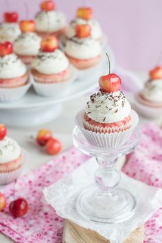 cupcakes with white frosting and cherries are on the table next to each other