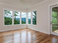 an empty room with wood flooring and three large windows overlooking the trees in the distance