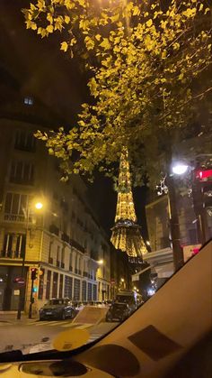 the eiffel tower is lit up at night with autumn leaves on it's branches