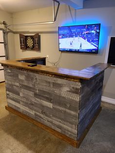 a large tv mounted to the wall above a wooden bar in a basement with lights on