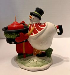 a ceramic figurine holding a lit candle with a hat on it's head