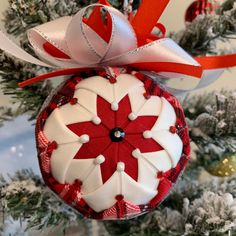 a red and white ornament hanging from a christmas tree with ribbon on it