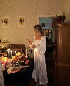 a woman standing in front of a table full of food and drinks with candles on it