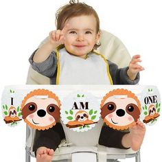 a baby sitting in a high chair with his hand up to the camera and smiling