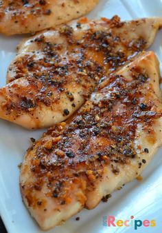 three pieces of chicken with seasoning on them sitting on a white platter, ready to be cooked