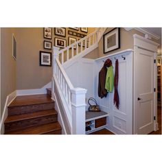 there is a coat rack under the stairs in this house with pictures on the wall