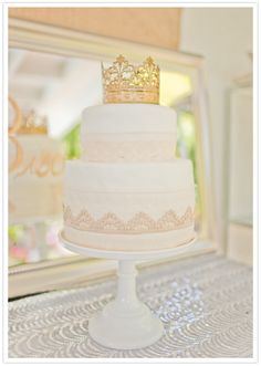 a three tiered cake with a crown on top sits on a table in front of a mirror