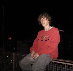 a young man sitting on top of a metal railing at night with his hands in his pockets